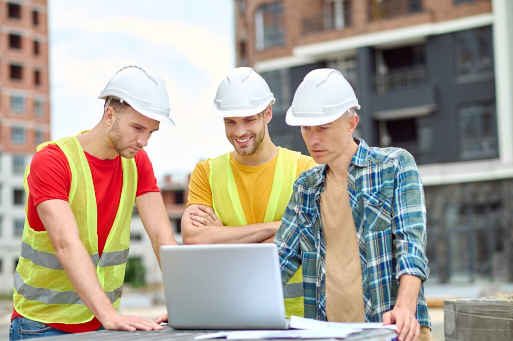 three men looking into laptop at construction site
